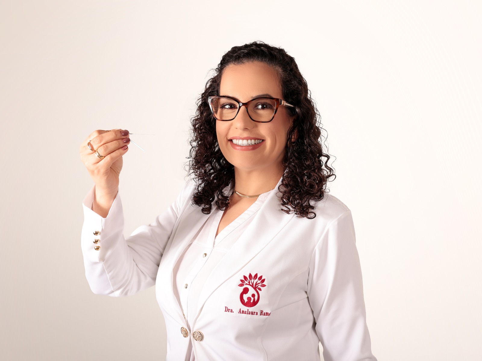 Dra. Analaura Ramos de jaleco, segurando uma agulha de acupuntura.