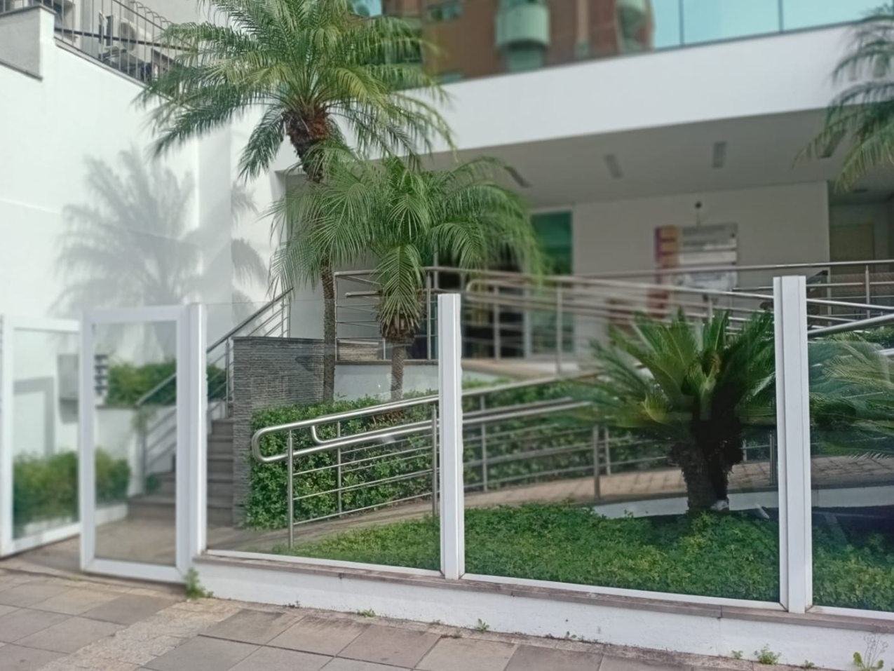 Entrada do prédio onde fica o consultório, com portão de vidro e jardim.