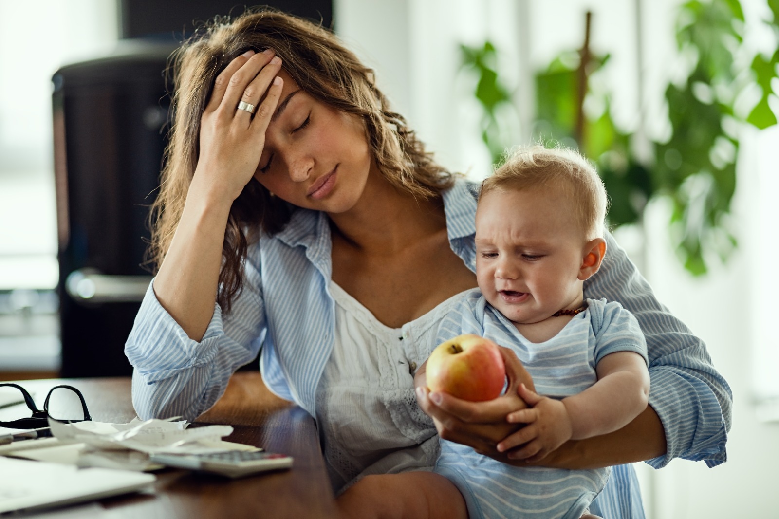 Mãe cansada segurando o bebê, que chora diante de uma maçã