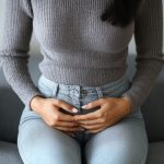A woman sits on a couch, cradling her stomach with a thoughtful expression.